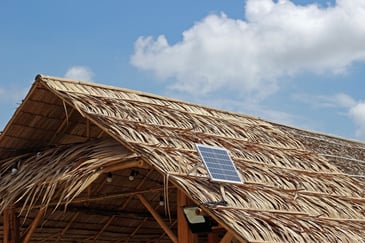 Thatched roof with a small solar panel installed on it under a blue sky with scattered clouds.