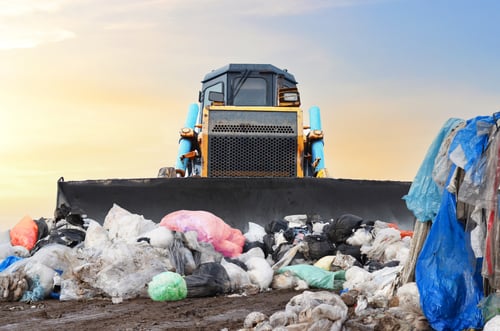 The sun rises over an immense landfill. A construction vehicle can be seen plowing through the hills of garbage.