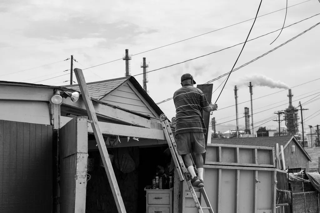 Photo taken by Pablo Unzueta in Los Angeles, California, featuring an adult male on a ladder with smokestacks in the background, displaying how pervasive pollution is in this community