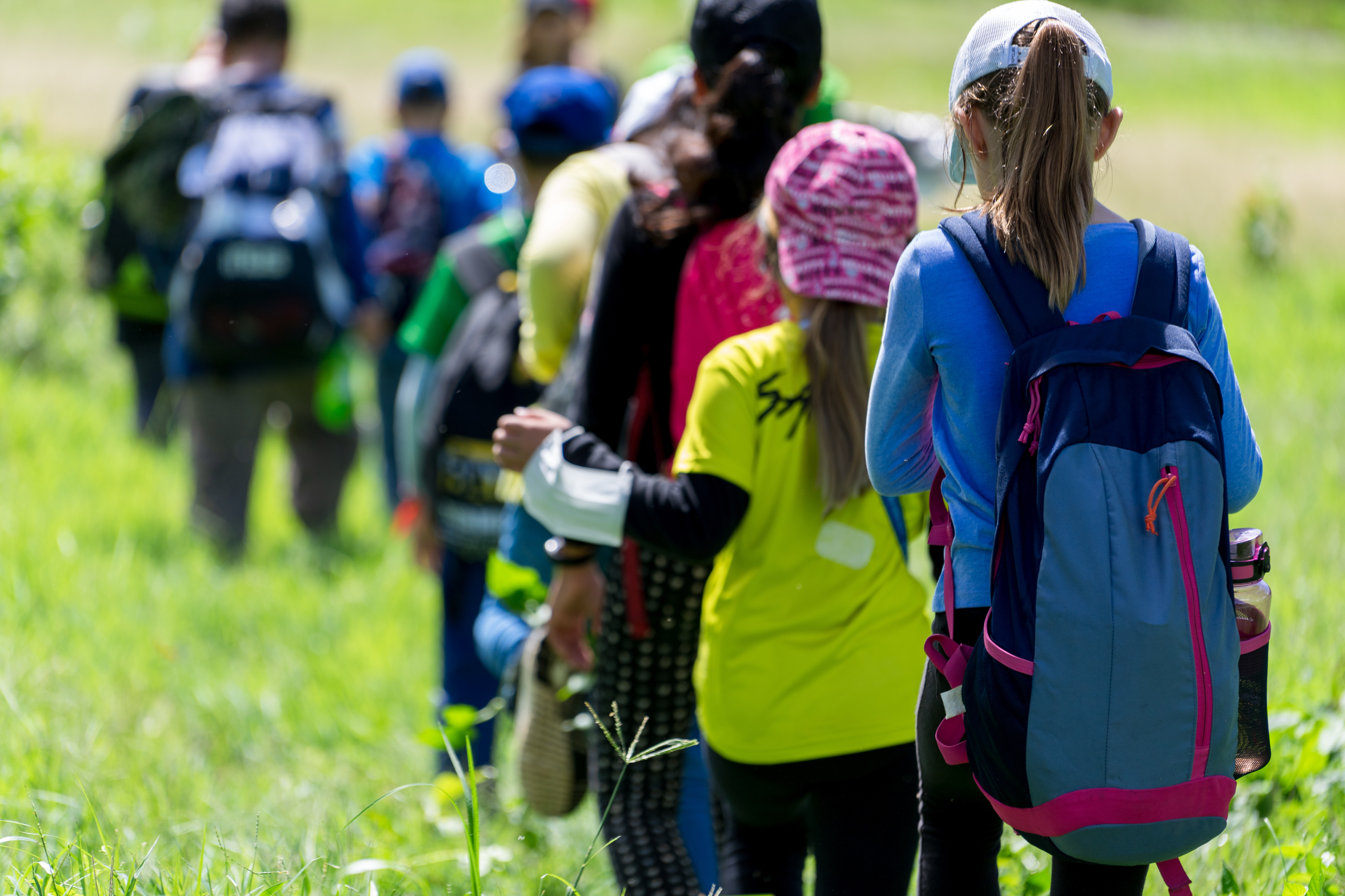 children with backpacks walking through grassy field